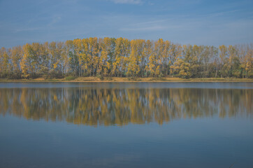 colors of autumn, yellow trees and blue pond in scenic countryside