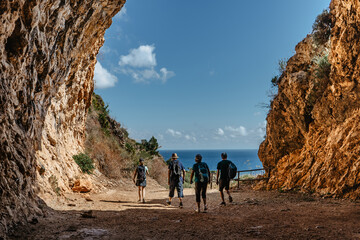 Silhouettes of family on active holiday back view.Group of two seniors and two adults trekking in rocky mountains,Sicily,Italy.Happy multi-generation family walking along coast.Enjoying time together - obrazy, fototapety, plakaty