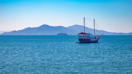 Obraz premium fishing boat in the background blue mountains on a sunny day in the city of Florianópolis, Brazil