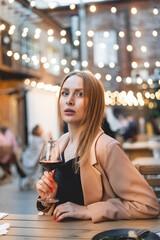 Blonde woman with wine glass. Lady in the elegant wear have luxury dinner outdoor. Cozy lights