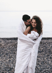 A couple in love are walking together hugging spend the night covered with a white blanket on the ocean beach on a romantic honeymoon in nature. Passionate man and woman of mixed diverse races