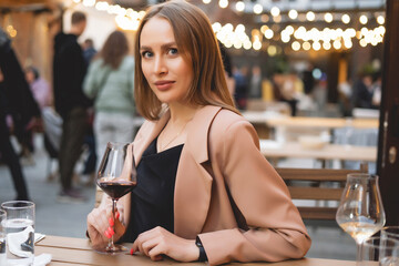 Blonde woman with wine glass. Lady in the elegant wear have luxury dinner outdoor. Cozy lights