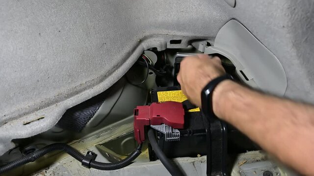 Car battery replacement with housing in the rear trunk. The electrician removes a plastic bulkhead to free access to the car's service battery.