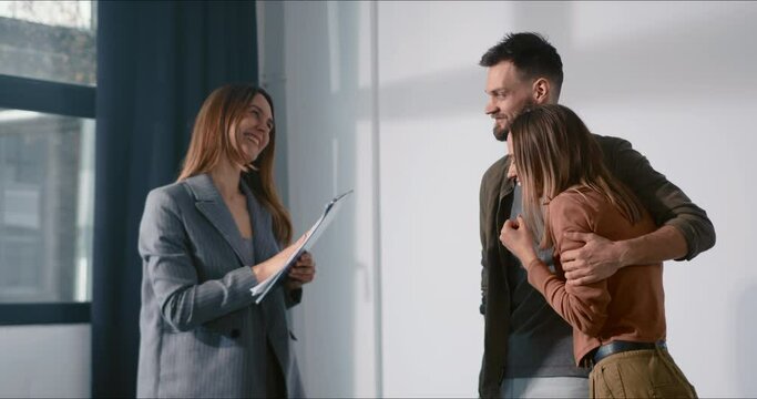 Buying real estate. Happy young couple making deal with smiling female realtor taking keys and celebrating new apartment