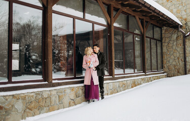 Lovely couple hugging and laughing outdoors in winter. Couple posing near a beautiful building. Winter wedding of a stylish beautiful young couple bride and groom