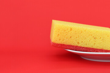 A yellow sponge lies in a white plate on a red background, a place for placing text
