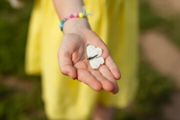 Hand of a girl in the yellow dress with a butterfly in it. Closeup