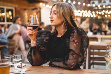 Blonde woman with wine glass. Lady in the elegant wear have luxury dinner outdoor. Cozy lights