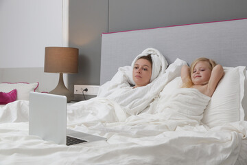 Mother and her toddler girl watching cartoons on laptop in bed