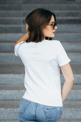 Stylish brunette girl wearing white t-shirt and glasses posing against street , urban clothing...