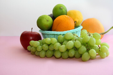 Naklejka na ściany i meble fresh fruit in the basket apple, lime, avocado, lemon, orange, grapes on a light pink background