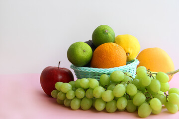 fresh fruit in the basket apple, lime, avocado, lemon, orange, grapes on a light pink background