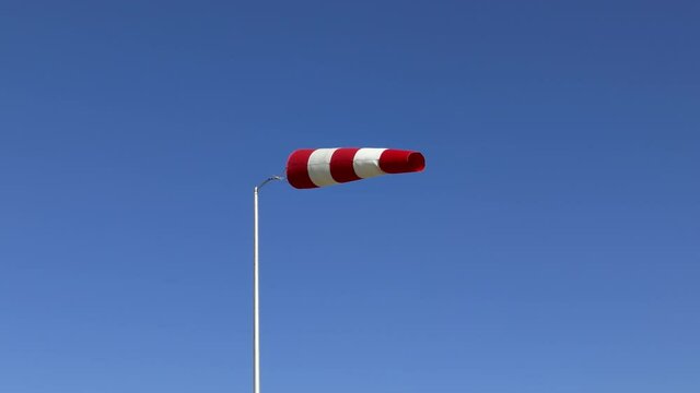 Windsock flutters in a strong wind showing wind direction and speed against perfect blue sky on clear summer day.