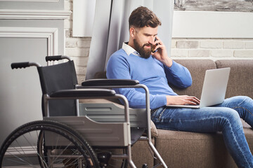 Disabled businessman sitting on a couch, working on a laptop, talking on a phone