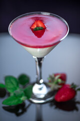 Panna Cotta in cocktail glass with strawberry jam and mints on a black background with reflections 