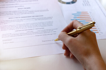 Young business woman signs a business contract on the background of economic charts while sitting at the table. Business and finance concept. Selective focus.