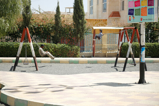Father and daughter swinging in a public park. kid rises high and looks forward with optimism and freedom, man filled with sadness and melancholy, war in Yemen. yemen kids