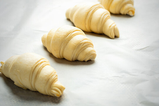 Uncooked croissants pastry roll in a baking tray ready to be baked. Selective focus.