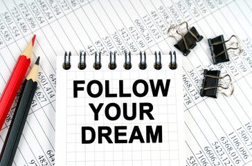 On the table are reports, pencils and a notebook with the inscription - FOLLOW YOUR DREAM