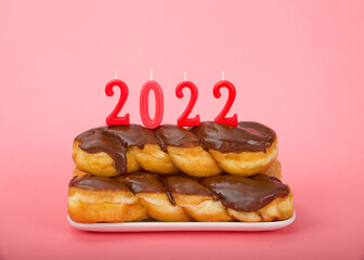 Chocolate frosted glazed twist donuts stacked on a rectangular plate pink background with pink 2022 candles. Happy New Year theme.