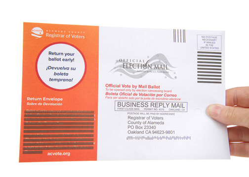 Alameda, CA - August 6, 2021: Caucasian hand holding mail in ballot, isolated on white. Gubernatorial recall election ballots sent out to all registered voters in California.