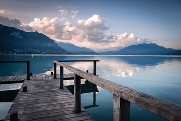 Fototapeta na wymiar Natural landscape of Lake Annecy with colorful clouds at sunrise, Alps mountains in the background and a small wooden pier in the foreground, France