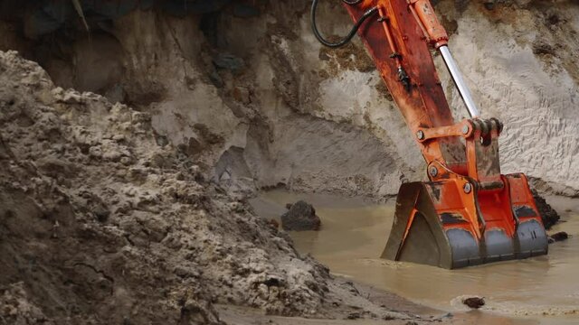 Close-up of a large excavator bucket scooping mud and water from a pit at a construction site