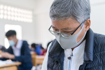 Asian Female teacher wearing white face mask safety during COVID-19 pandemic coronavirus epidemic standing front greenboard classroom at school when students quarantine. Healthcare on Education ideas