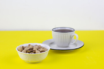 Pistachios in a white plate on a yellow background with a white cup of tea