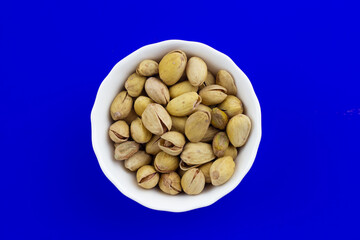 Pistachios in a white plate on blue background