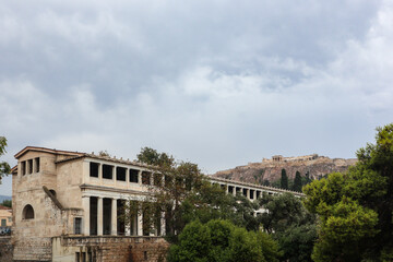 Fototapeta na wymiar Stoa of Attalos in greenery, Athens old city center architecture on gray day with epic clouds and view on Acropolis hill