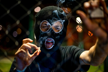 young man in balaclava looking at camera and blow smoke out. crime and violence, drugs, fashion,...