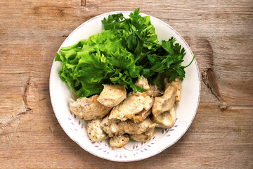 Chicken cream stew with green salad on white plate on wooden table background. Top view. Flat lay. Close up. Selective soft focus. Shallow depth of field. Text copy space.