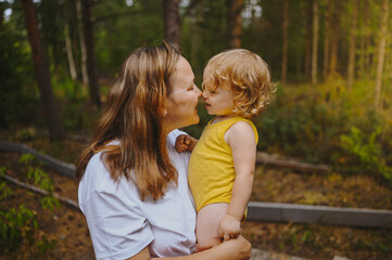 Little cute baby toddler girl blonde with curls on mother's arms. Mother and daughter playing spend time together outdoors at countryside front yard summertime. Healthy happy family childhood concept