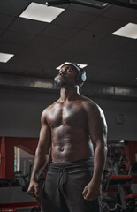 Obraz na płótnie Canvas Athletic african american man in wireless headphones with closed eyes and naked torso standing in gym