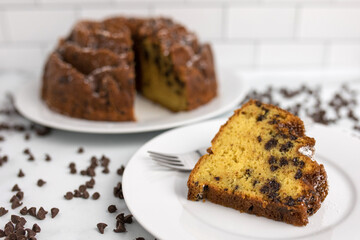 An ornate and decorative homemade and fresh chocolate chip bundt cake with a clice cut out on top of a serving plate