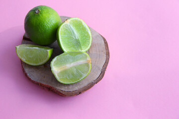 Lime and juicy lime slices on a wooden plate on a bright background
