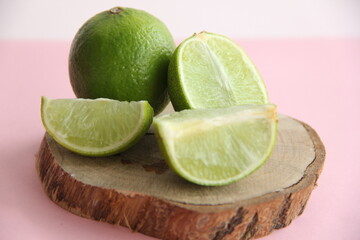 Lime and juicy lime slices on a wooden plate on a bright background
