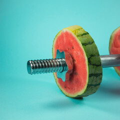 Weightlifting dumbbells made of steel bar and watermelon slices. On trendy pastel background....