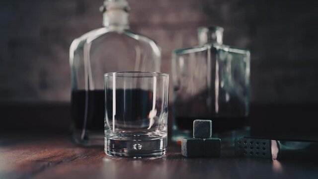 Barman pouring golden whiskey, cognac or brandy from bottle into glass on table. Bartender pouring glass of alcohol drink bourbon, rum and adding ice cooling stones.