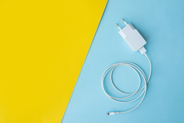 Mobile charger and USB Cable on blue and yellow background. Top view. 