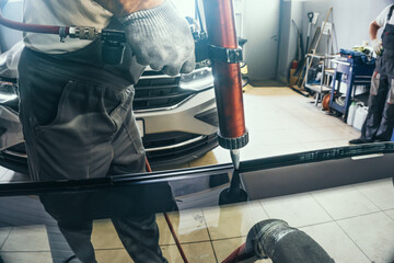 Install auto windscreen on car process. Service man applies glue using special equipment to new...