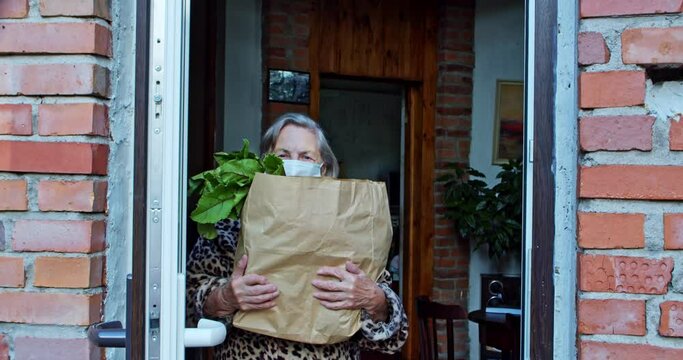 senior adult receiving food delivery at home.portrait of a confused isolated pensioner in a protective mask with a bag of food. a smart service for delivering fresh food to an elderly recipient