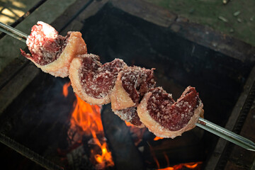 Raw rump steak seasoned with coarse salt on the grill with fire, the traditional Churrasco Gaúcho, Brazilian barbecue.