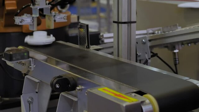 Close up: pick and place robotic arm manipulator moving plastic detail on conveyor belt at modern robot trade show, exhibition. Manufacturing, quality control, industrial, automated technology concept