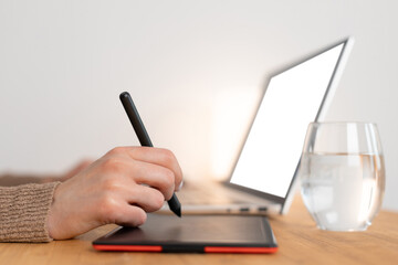 Graphic designer work with digital graphic tablet and laptop. Wooden workspace. Woman freelancer work from home office. Selective focus on hand with pencil, blurred background. Close up photo.