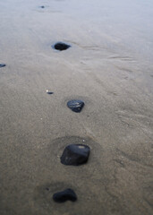 Fototapeta na wymiar Line of black stones on beach in the sand with small amounts of water by the ocean