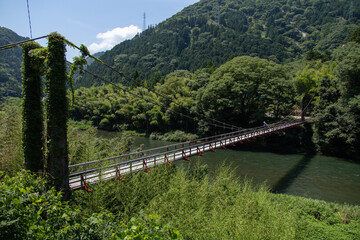 Fototapeta na wymiar 山間を流れる川に架けられた木製の吊り橋