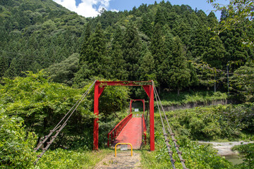 Fototapeta na wymiar 山間を流れる川に架けられた鉄製の赤い吊り橋