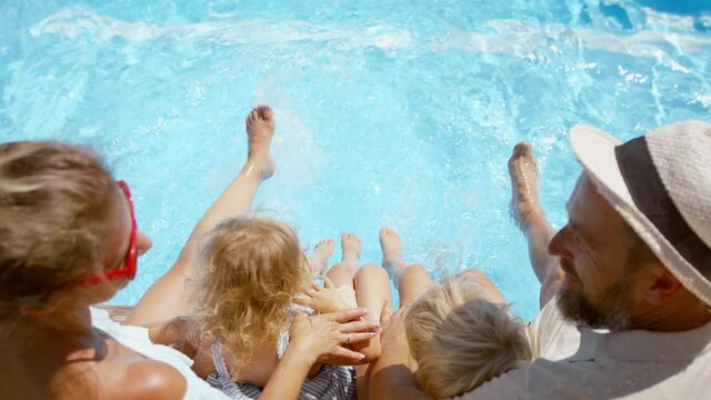 Top view of beautiful family sitting on the edge of the pool and having fun together.